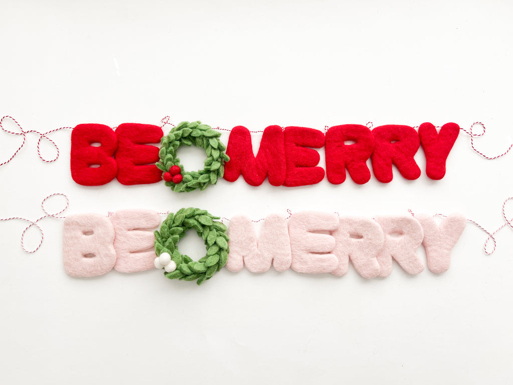 A decorative felt garland with the text 'BE MERRY' in red and pale pink colors, interspersed with green felt wreaths with white or red berries.